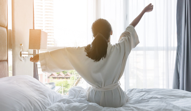 Woman stretching in the morning on the side of her bed.